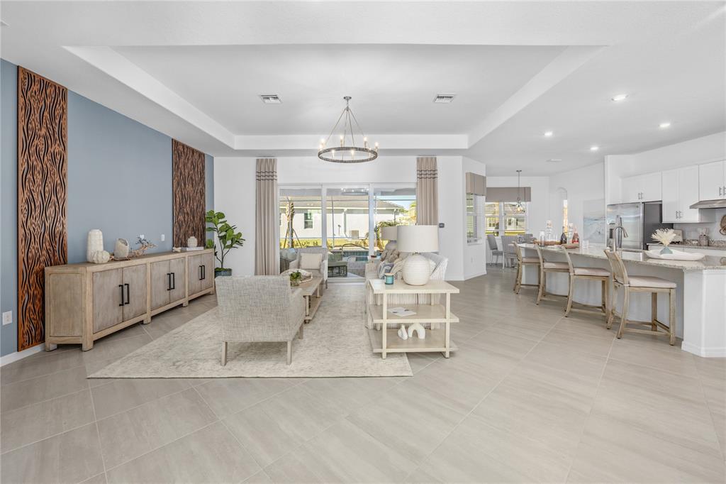 An open-concept living room and kitchen feature light tile flooring, a tray ceiling, and decorative wall panels — 18845 CHERRYSTONE WAY, LAKEWOOD RANCH, FL