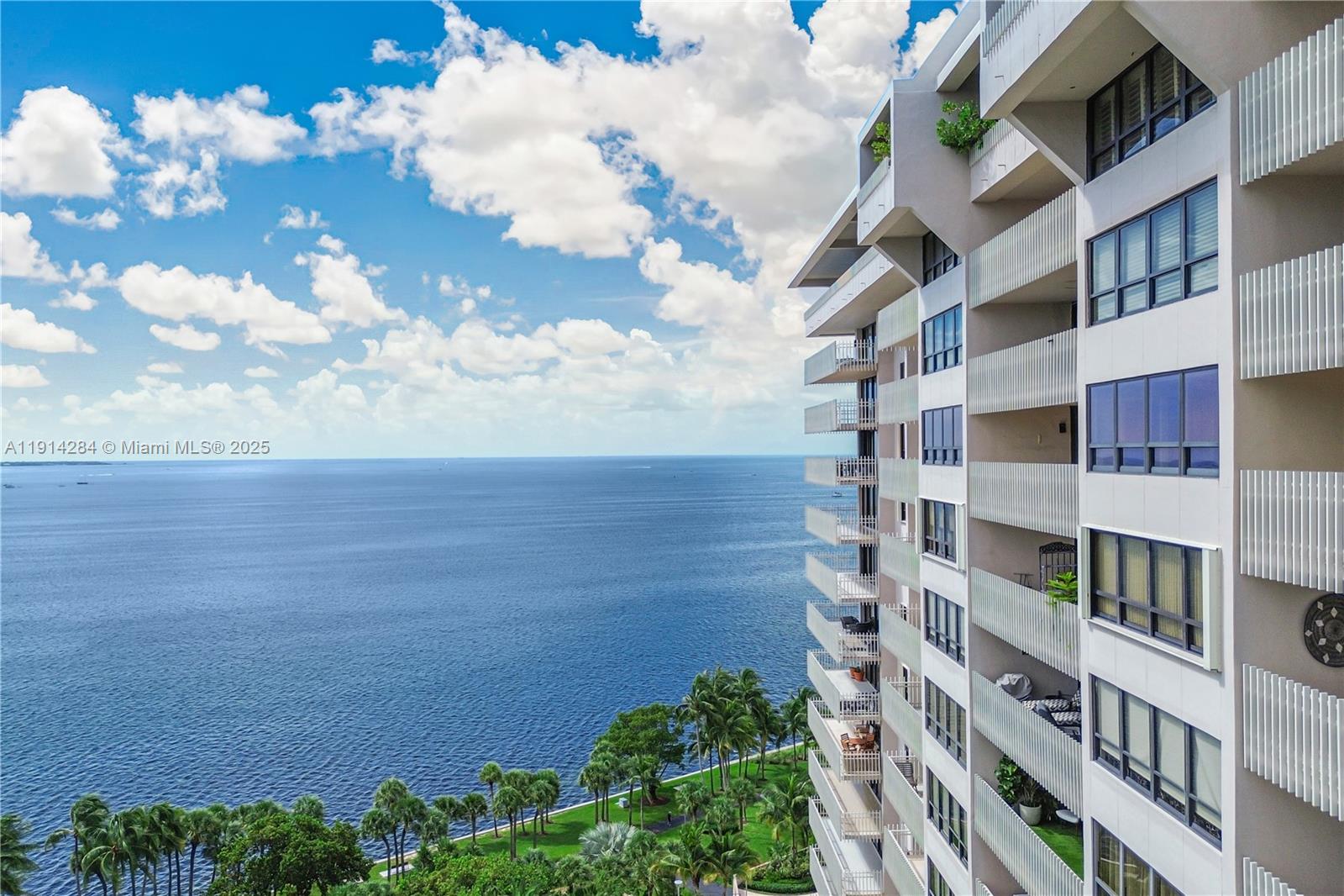 An exterior view of a high-rise building overlooking the ocean and palm trees — 2 Grove Isle Dr # B1507, Miami FL 33133, MIAMI, FL