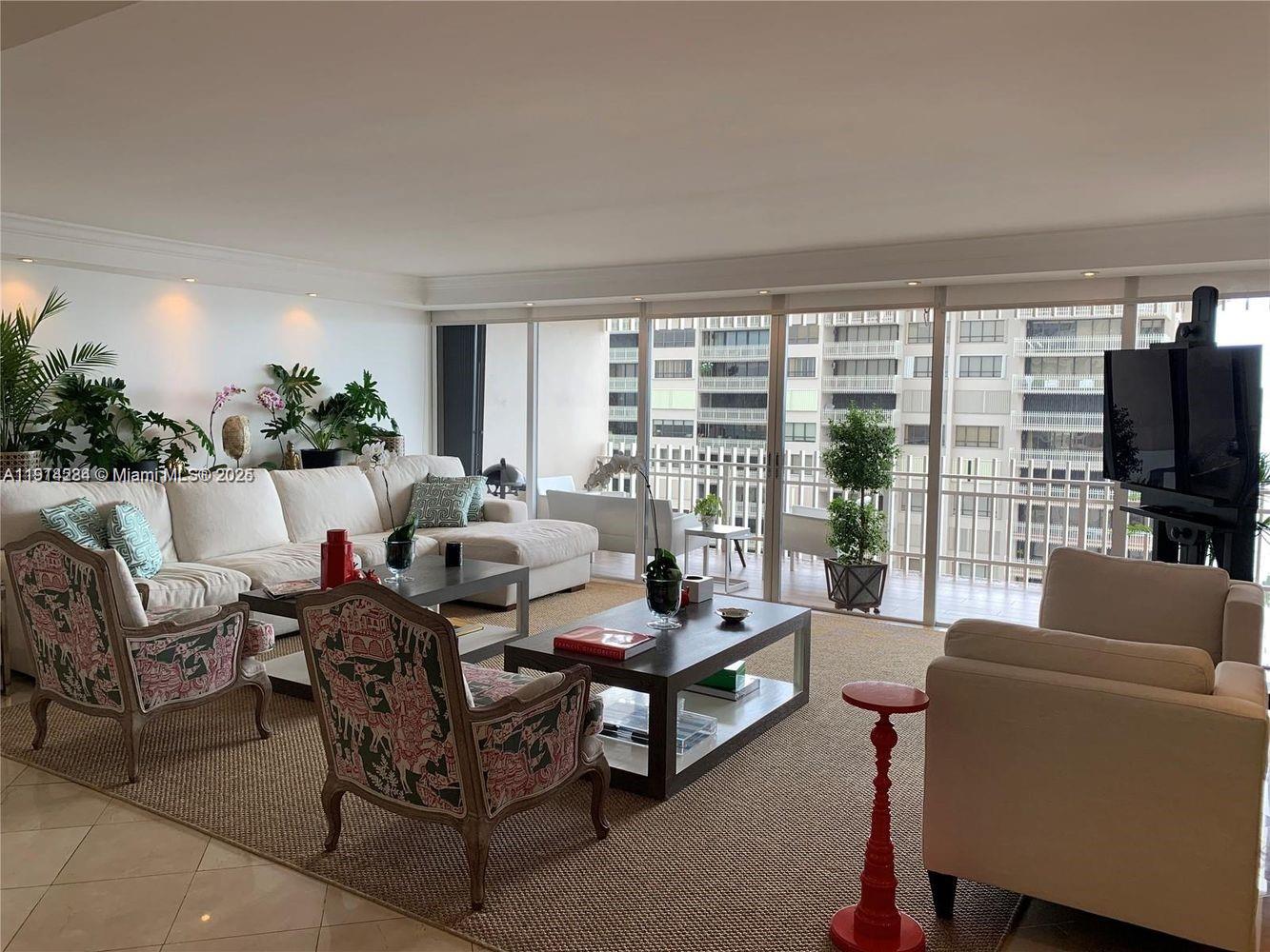 A living room features a white sectional sofa, patterned armchairs, and a balcony with city views — 2 Grove Isle Dr # B1507, Miami FL 33133, MIAMI, FL