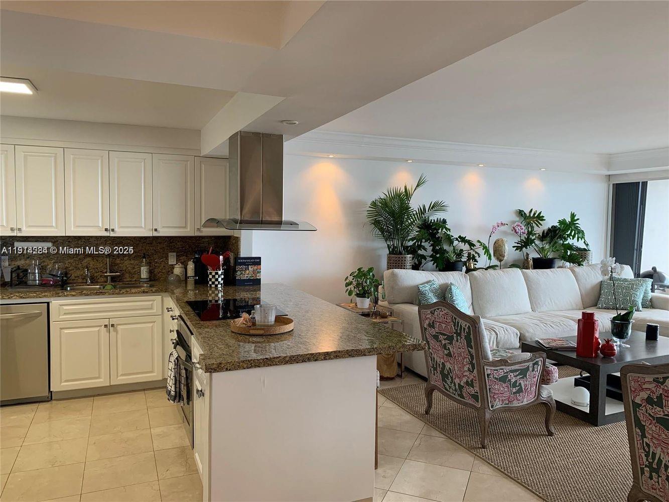 An open-concept kitchen with granite countertops and white cabinets overlooks a living room area — 2 Grove Isle Dr # B1507, Miami FL 33133, MIAMI, FL