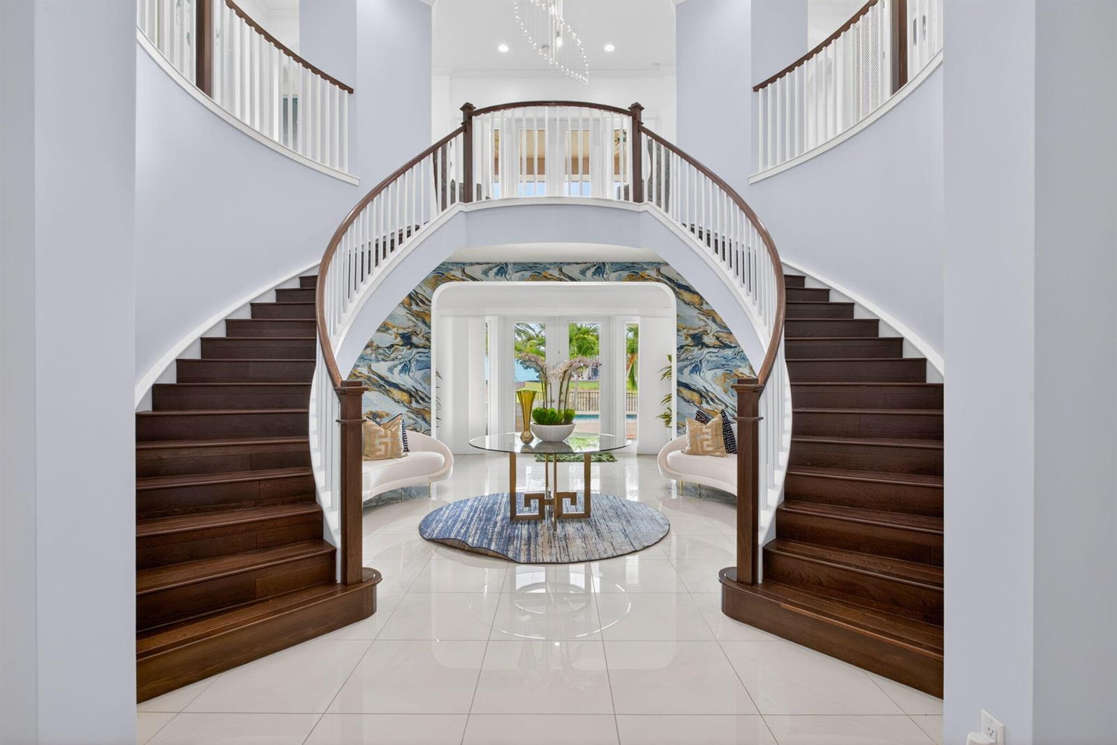 A grand foyer features a double curved staircase, white tile floors, and a central table — 9080 Vista Way, Parkland FL 33076, PARKLAND, FL