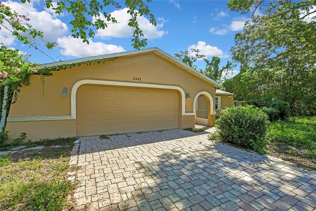 A tan house exterior features a two-car garage and a paved driveway — 2441 DUSTIN CIRCLE, SPRING HILL, FL