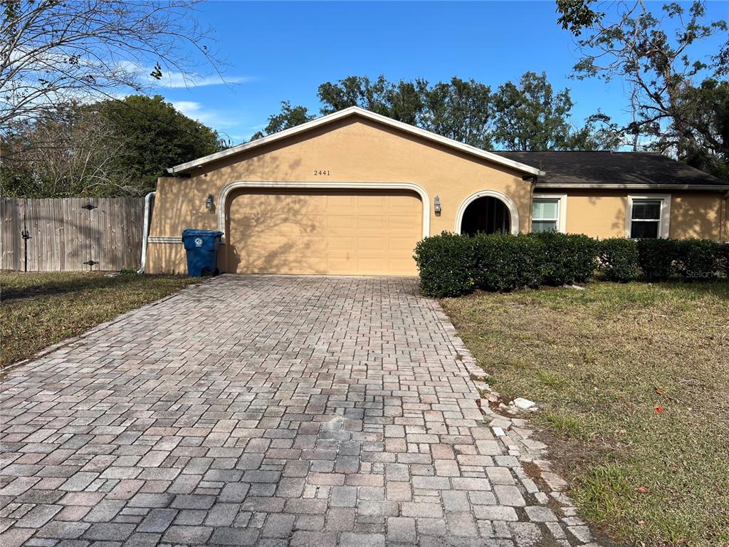 A tan single-story house features a two-car garage and a paved driveway — 2441 DUSTIN CIRCLE, SPRING HILL, FL