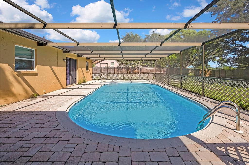 A rectangular swimming pool with a screen enclosure sits on a brick paver patio — 2441 DUSTIN CIRCLE, SPRING HILL, FL