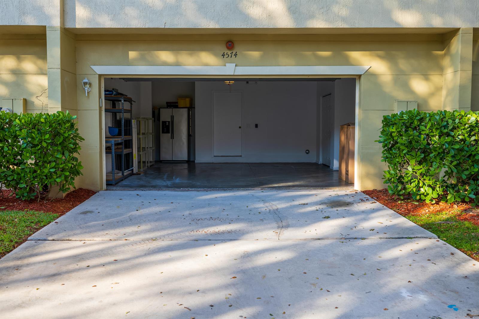 An open garage with a concrete driveway, storage shelving, and a refrigerator inside — 4574 Danson Way, Delray Beach FL 33445, DELRAY BEACH, FL