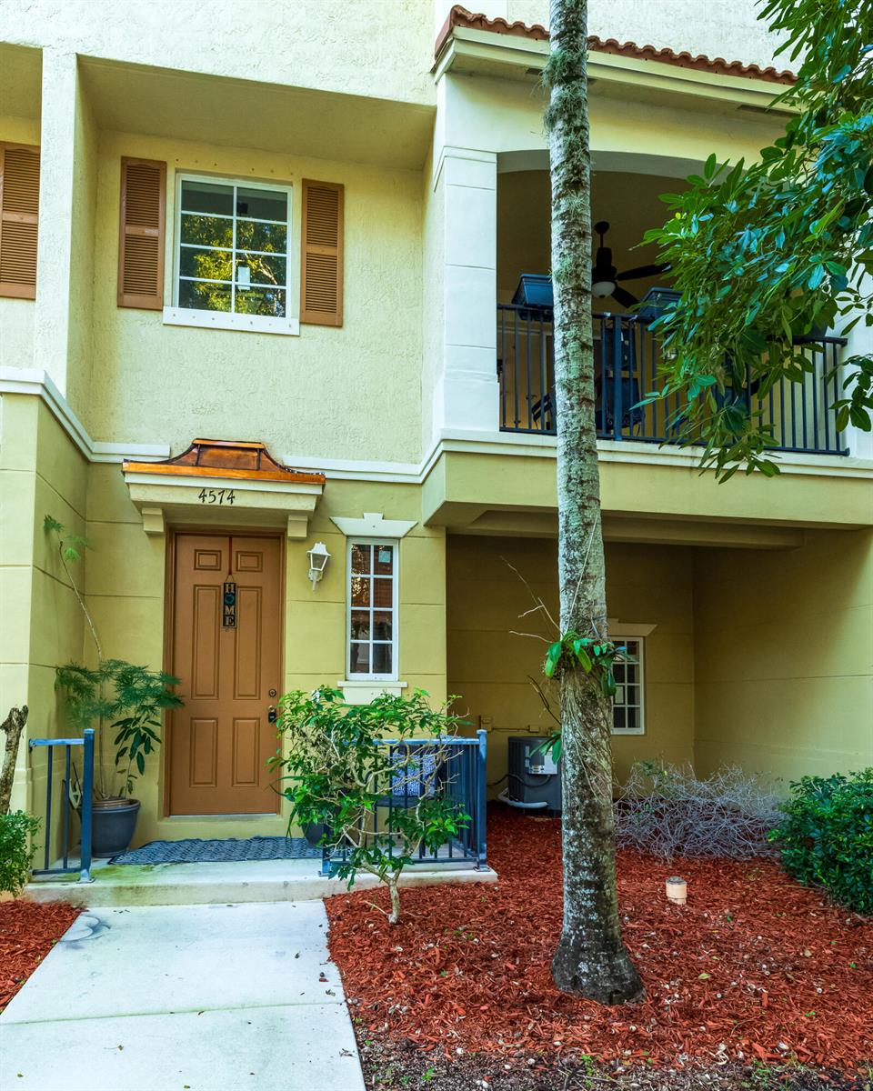 The exterior of a two-story townhouse features a tan door, a balcony, and landscaping — 4574 Danson Way, Delray Beach FL 33445, DELRAY BEACH, FL