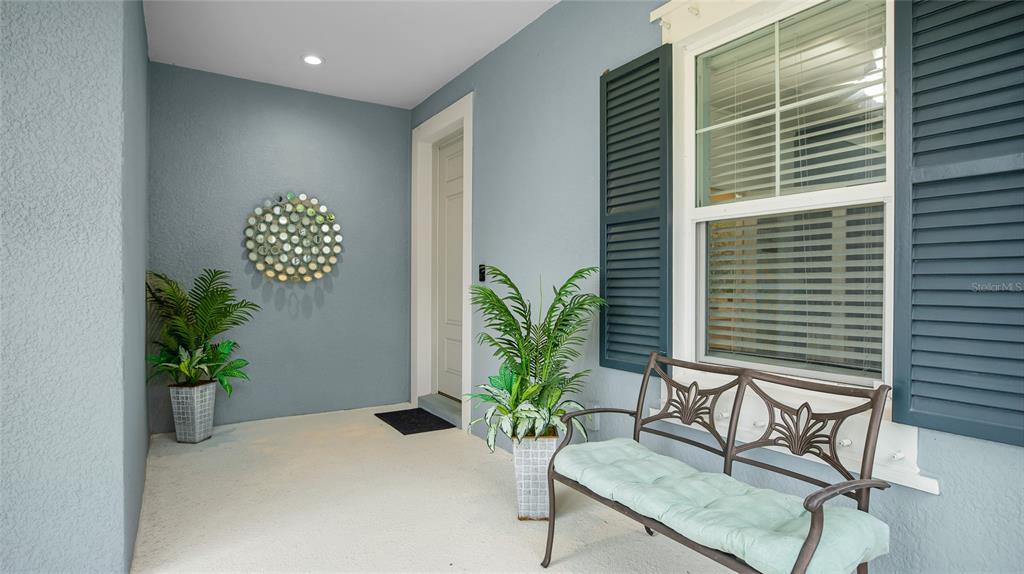 A covered front porch features a bench, two potted plants, and a circular wall decoration — 10601 FALLING LEAF COURT, PARRISH, FL