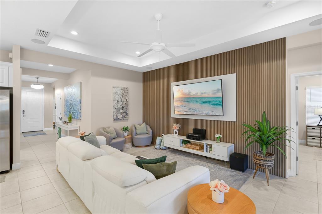A living room features a white sofa, a television on a slatted wood accent wall — 10601 FALLING LEAF COURT, PARRISH, FL