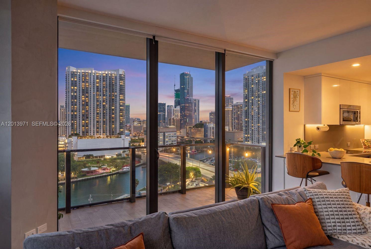 A living room with a balcony overlooks a city skyline and a river at sunset — 88 SW 7th St # 1012, Miami FL 33130, MIAMI, FL