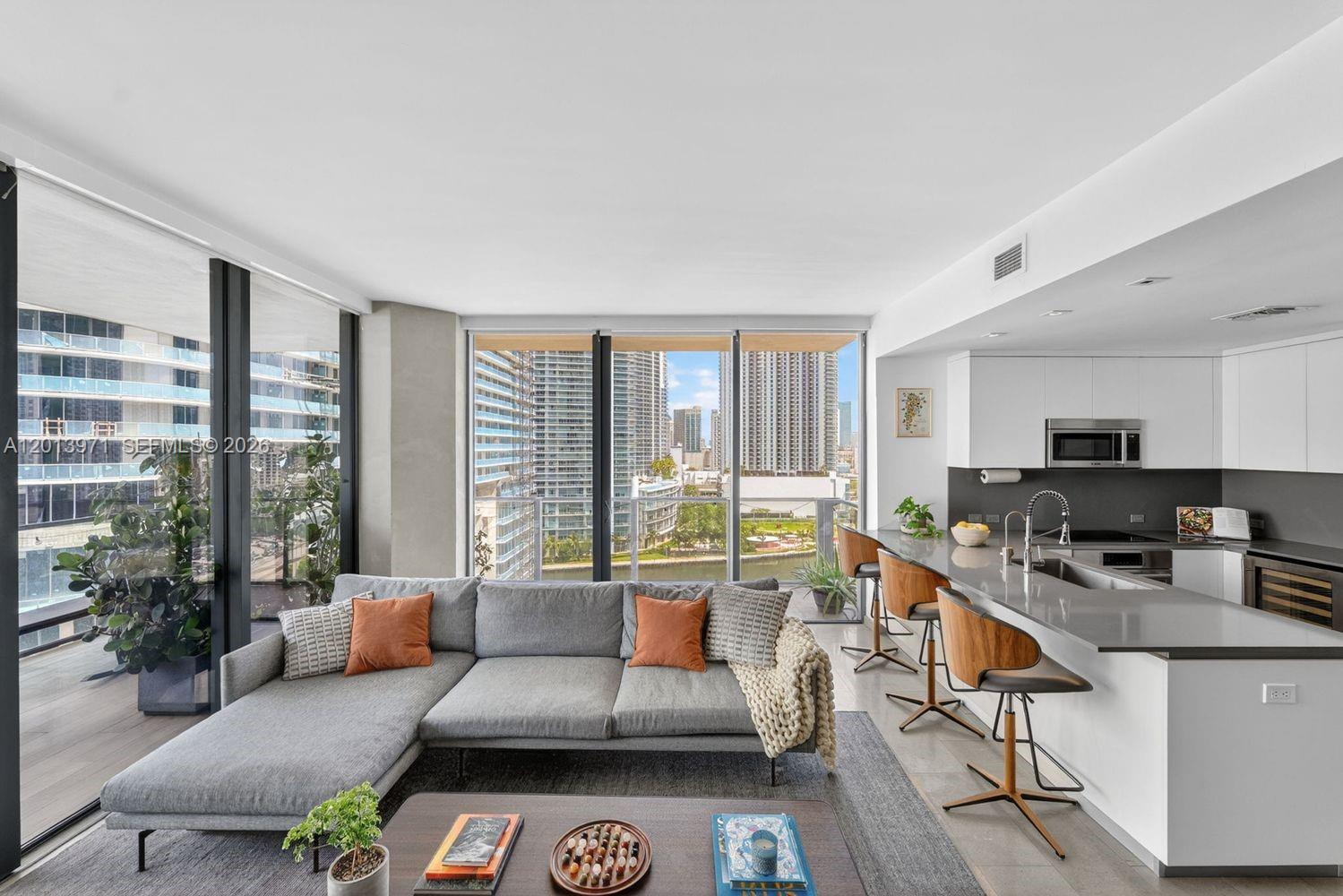 A modern living room and kitchen area features a gray sectional sofa and city views — 88 SW 7th St # 1012, Miami FL 33130, MIAMI, FL