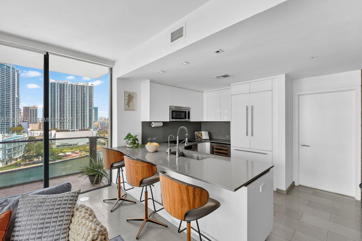 A modern kitchen features white cabinetry, gray countertops, a breakfast bar, and floor-to-ceiling windows — 88 SW 7th St # 1012, Miami FL 33130, MIAMI, FL