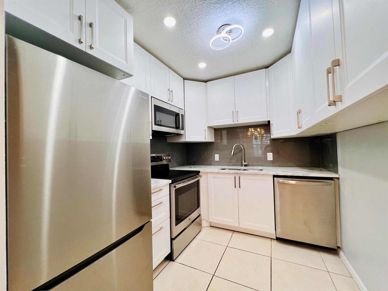 A kitchen featuring white cabinets, stainless steel appliances, a gray backsplash, and light-colored floor tiles — 74 Berkshire C, West Palm Beach FL 33417, WEST PALM BEACH, FL