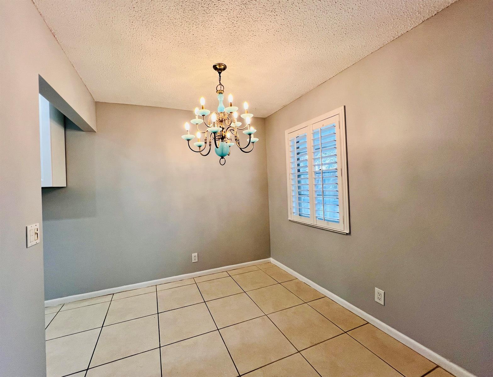 An empty dining room features beige tile flooring, gray walls, and a blue chandelier — 74 Berkshire C, West Palm Beach FL 33417, WEST PALM BEACH, FL