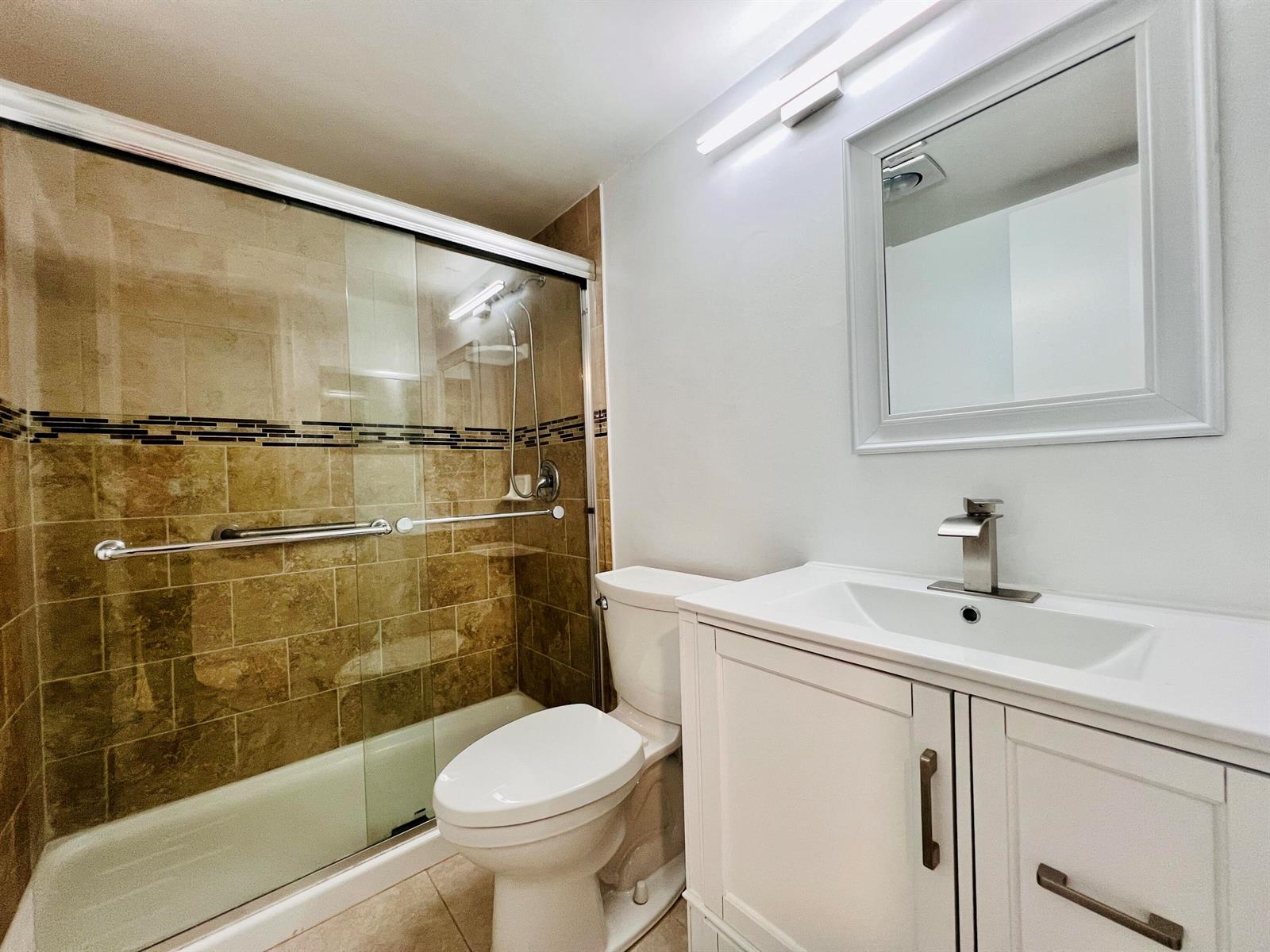 A bathroom features a tiled walk-in shower, a white vanity, and a toilet — 74 Berkshire C, West Palm Beach FL 33417, WEST PALM BEACH, FL
