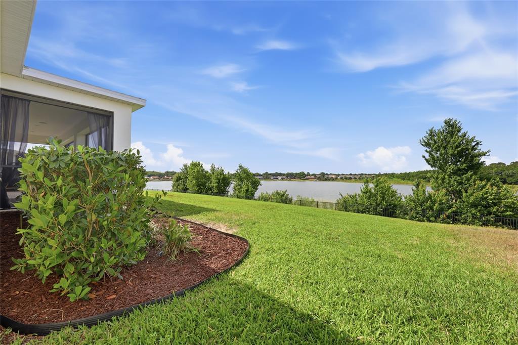 A grassy backyard with a landscaped shrub bed overlooks a lake and distant houses — 1383 WATERVIEW RIDGE CIRCLE, APOPKA, FL