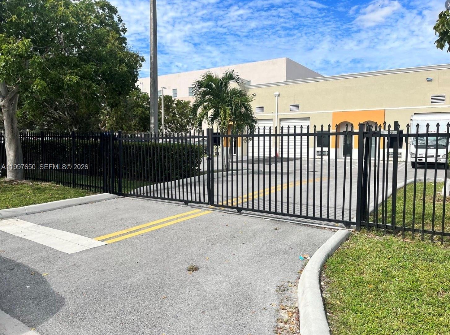 A black metal gate secures the entrance to a paved parking lot in front of buildings — 14911 SW 137th St # 14911, FL 33196, FL