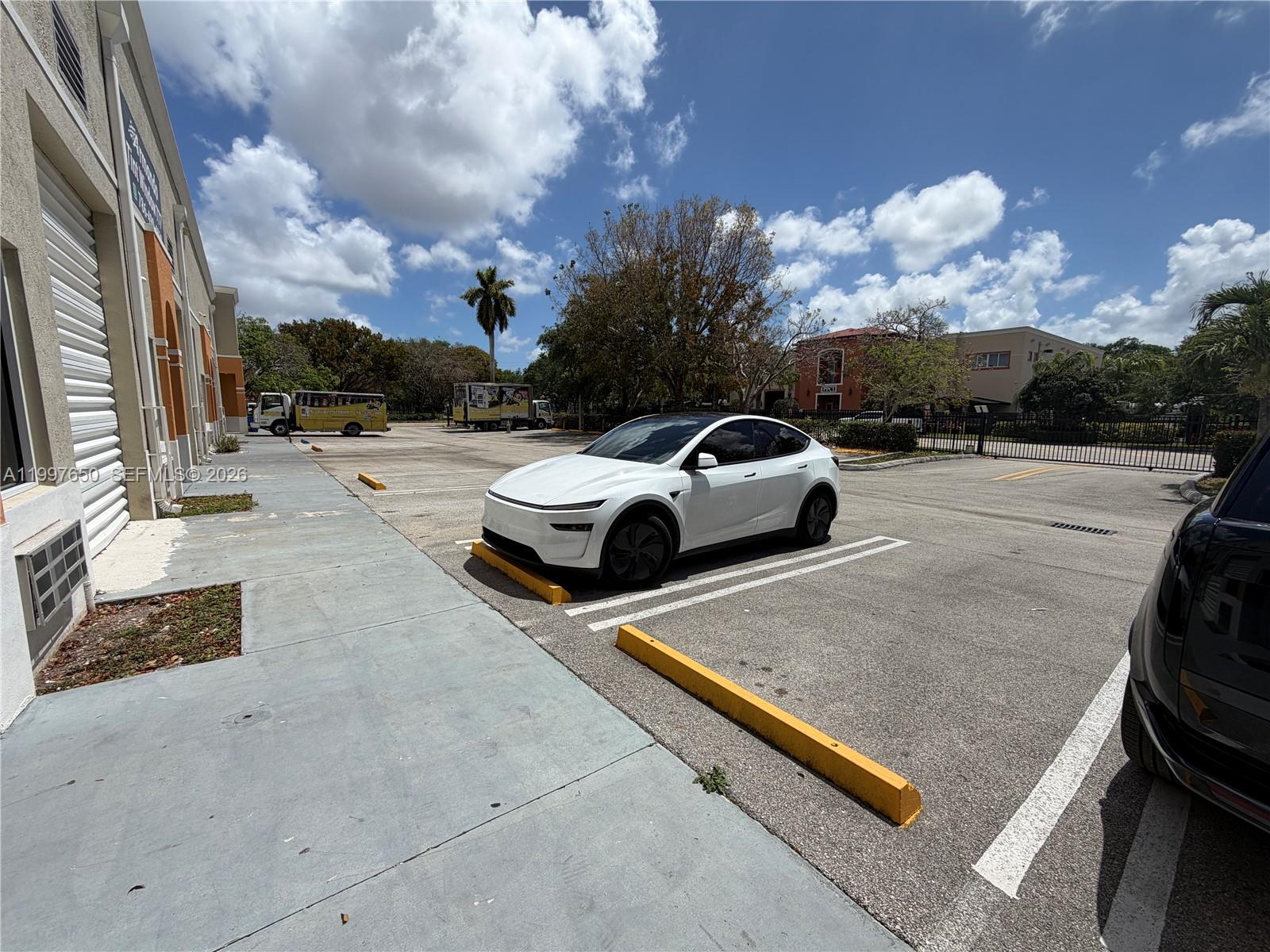 A white Tesla is parked in an outdoor parking lot next to a commercial building — 14911 SW 137th St # 14911, FL 33196, FL