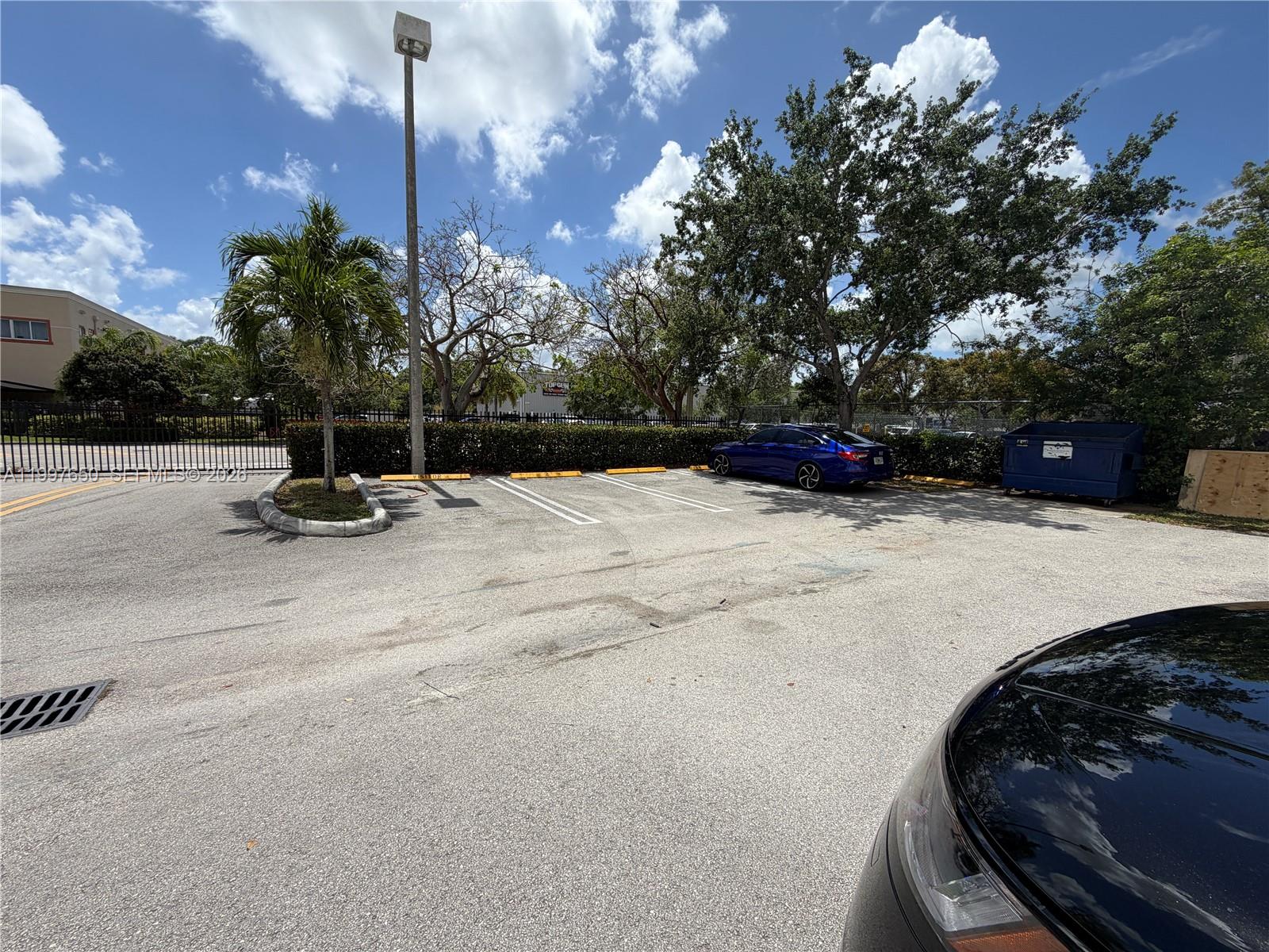 A paved parking lot features a blue sedan, a dumpster, and a palm tree — 14911 SW 137th St # 14911, FL 33196, FL