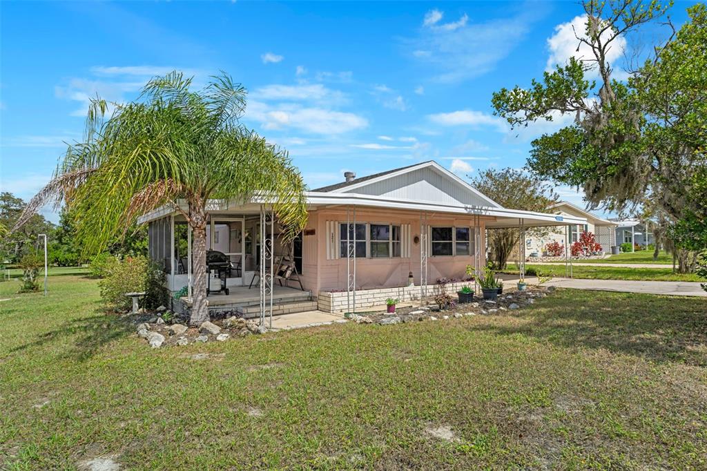 A single-story mobile home with a screened porch, metal carport, and a palm tree — 12107 ELDORADO AVENUE, BROOKSVILLE, FL