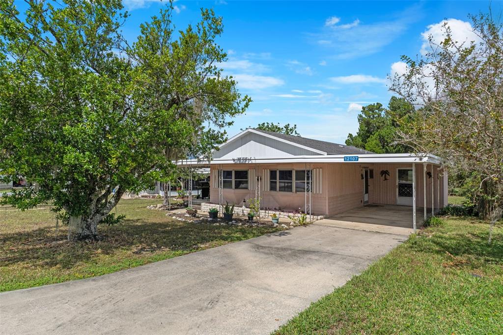 A single-story house with a carport and a concrete driveway sits on a grassy lot — 12107 ELDORADO AVENUE, BROOKSVILLE, FL