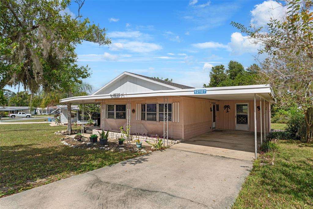 A single-story mobile home with a carport and light pink siding sits on a lawn — 12107 ELDORADO AVENUE, BROOKSVILLE, FL