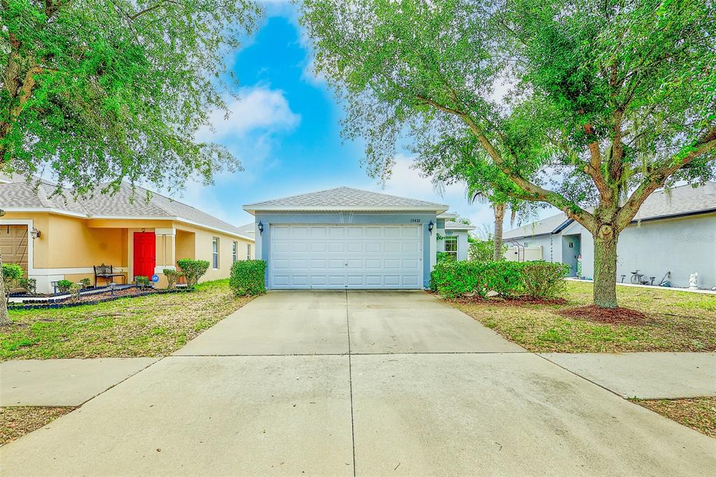 A single-story house with a blue garage, a concrete driveway, and trees in the front yard — 15410 QUAIL WOODS PLACE, RUSKIN, FL