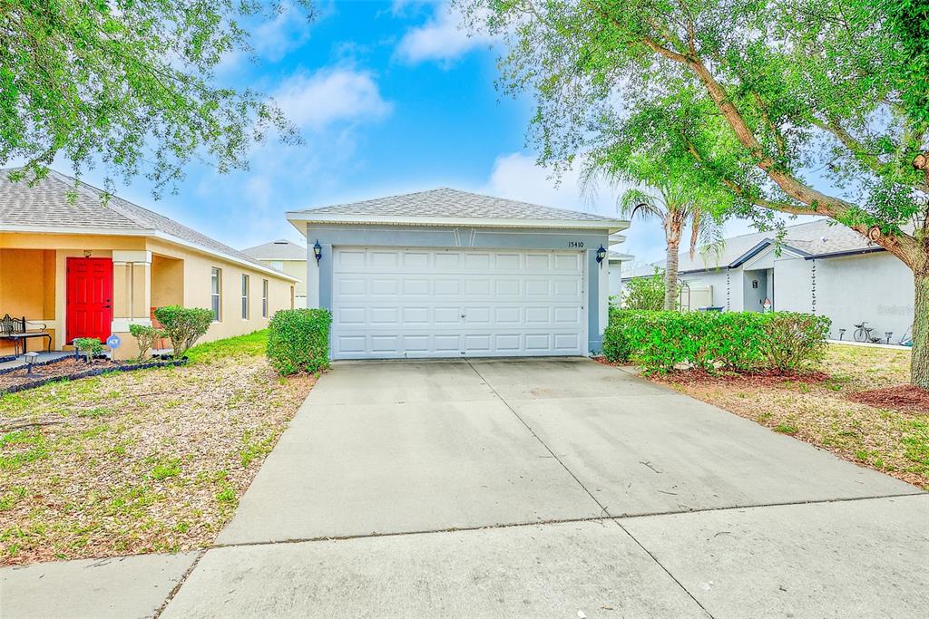 A single-story house exterior features a two-car garage, a concrete driveway, and a red door — 15410 QUAIL WOODS PLACE, RUSKIN, FL