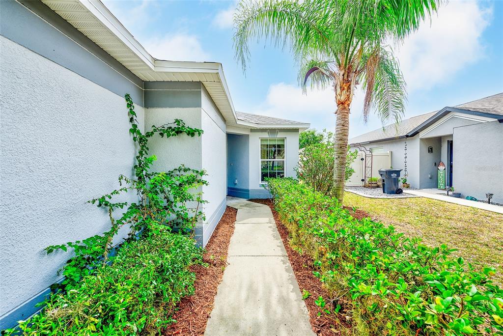 A concrete walkway leads to the front entrance of a house with a palm tree — 15410 QUAIL WOODS PLACE, RUSKIN, FL