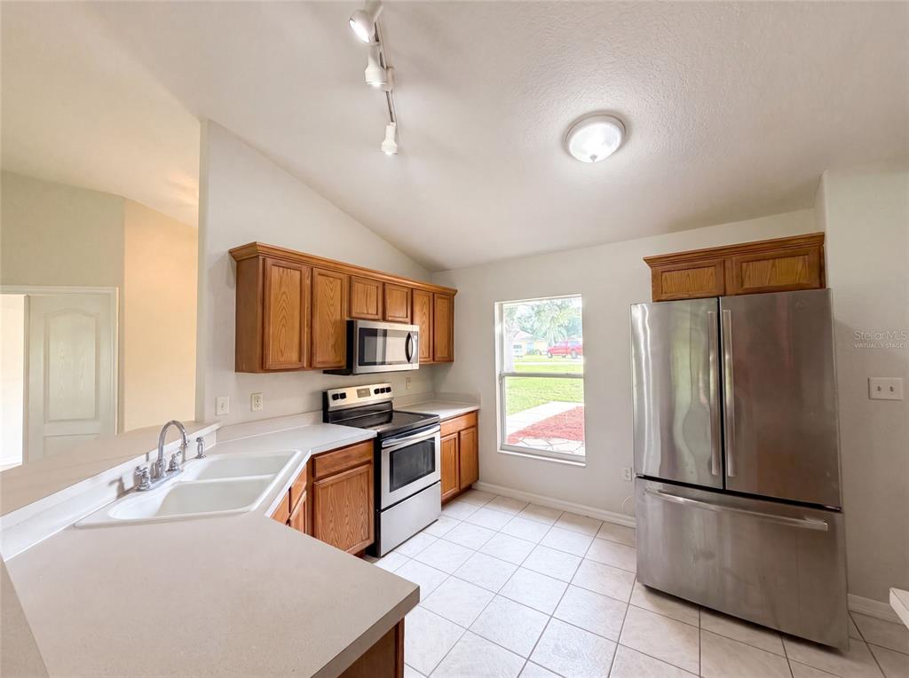 A kitchen features wood cabinets, stainless steel appliances, a double sink, and tile flooring — 314 DUPONT CIRCLE, HOWEY IN THE HILLS, FL