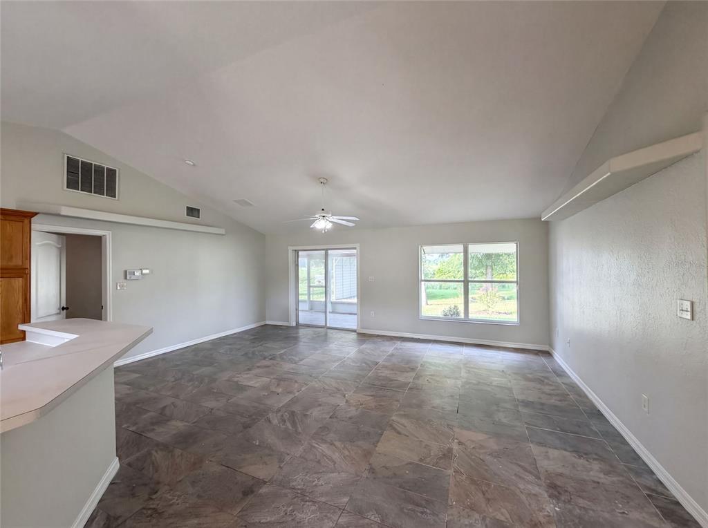 An open-concept living room features vaulted ceilings, tile flooring, and a sliding glass door — 314 DUPONT CIRCLE, HOWEY IN THE HILLS, FL