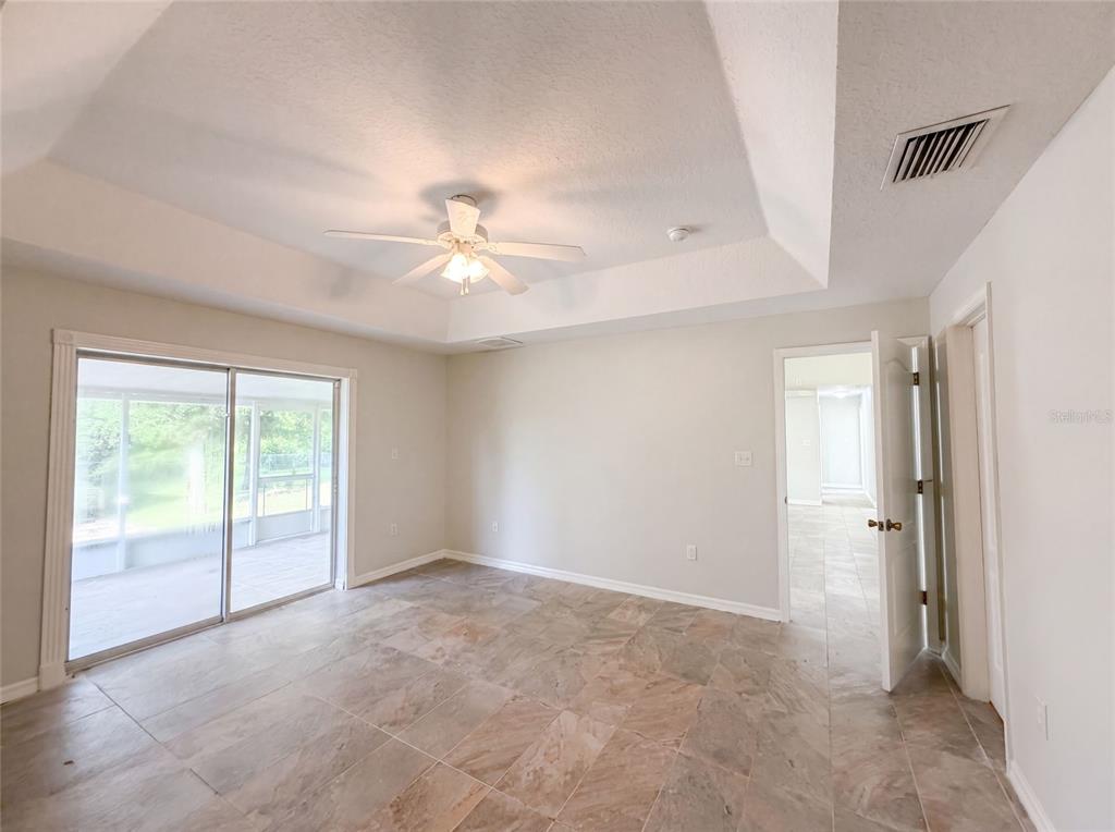 A bedroom with a tray ceiling, ceiling fan, tile flooring, and sliding glass patio doors — 314 DUPONT CIRCLE, HOWEY IN THE HILLS, FL