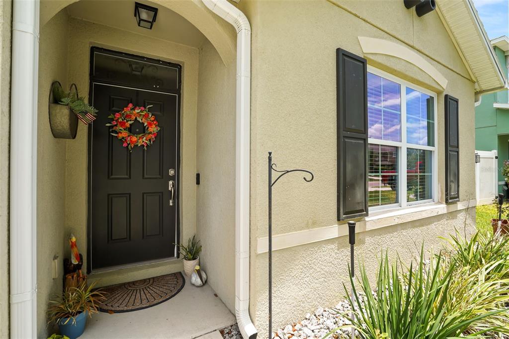 A front entryway features a dark door with a wreath, a window with shutters, and landscaping — 3422 BERKSHIRE WOODS TERRACE, DELTONA, FL