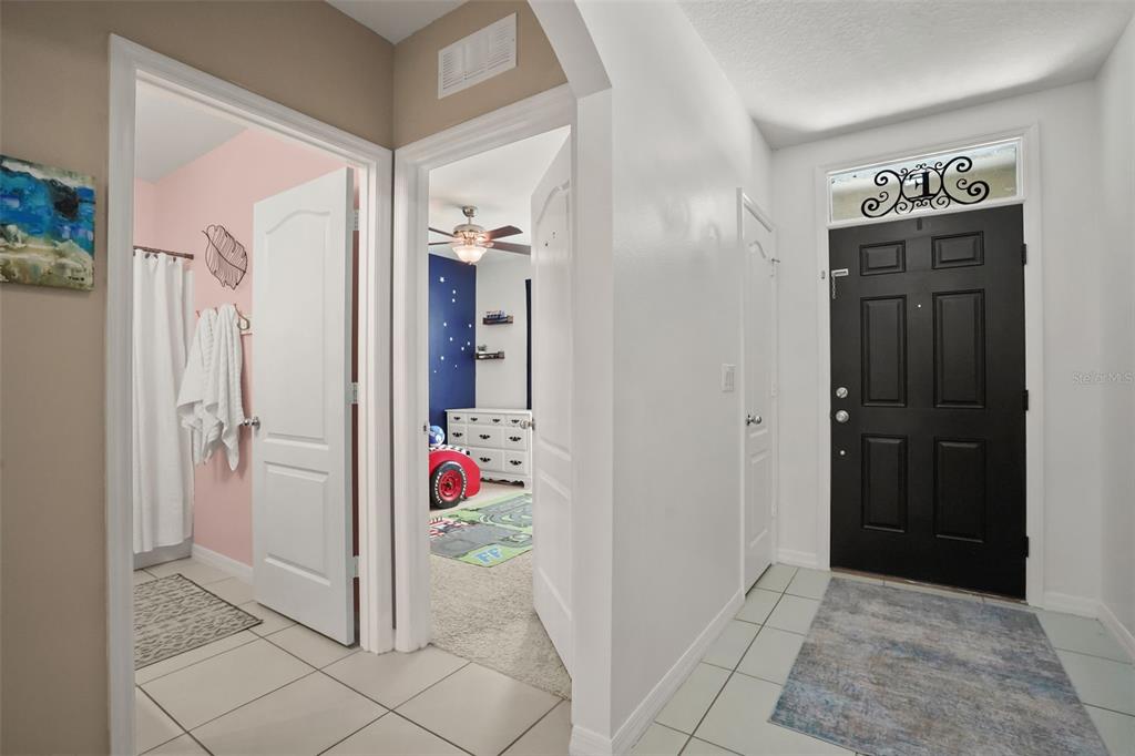 An entryway with a black front door, tiled floors, and doorways leading to two rooms — 3422 BERKSHIRE WOODS TERRACE, DELTONA, FL