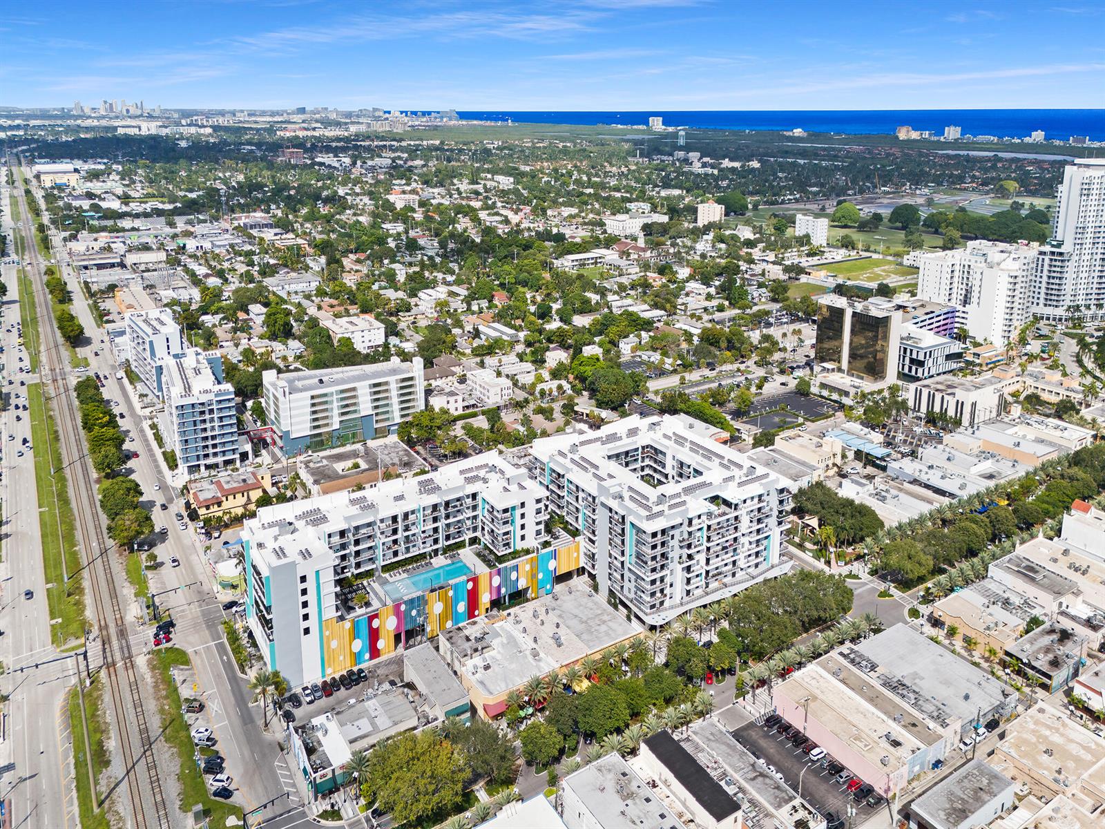 An aerial view shows modern apartment buildings with colorful accents situated near railroad tracks and city streets — 2001 Hollywood Boulevard, Hollywood FL 33020, HOLLYWOOD, FL