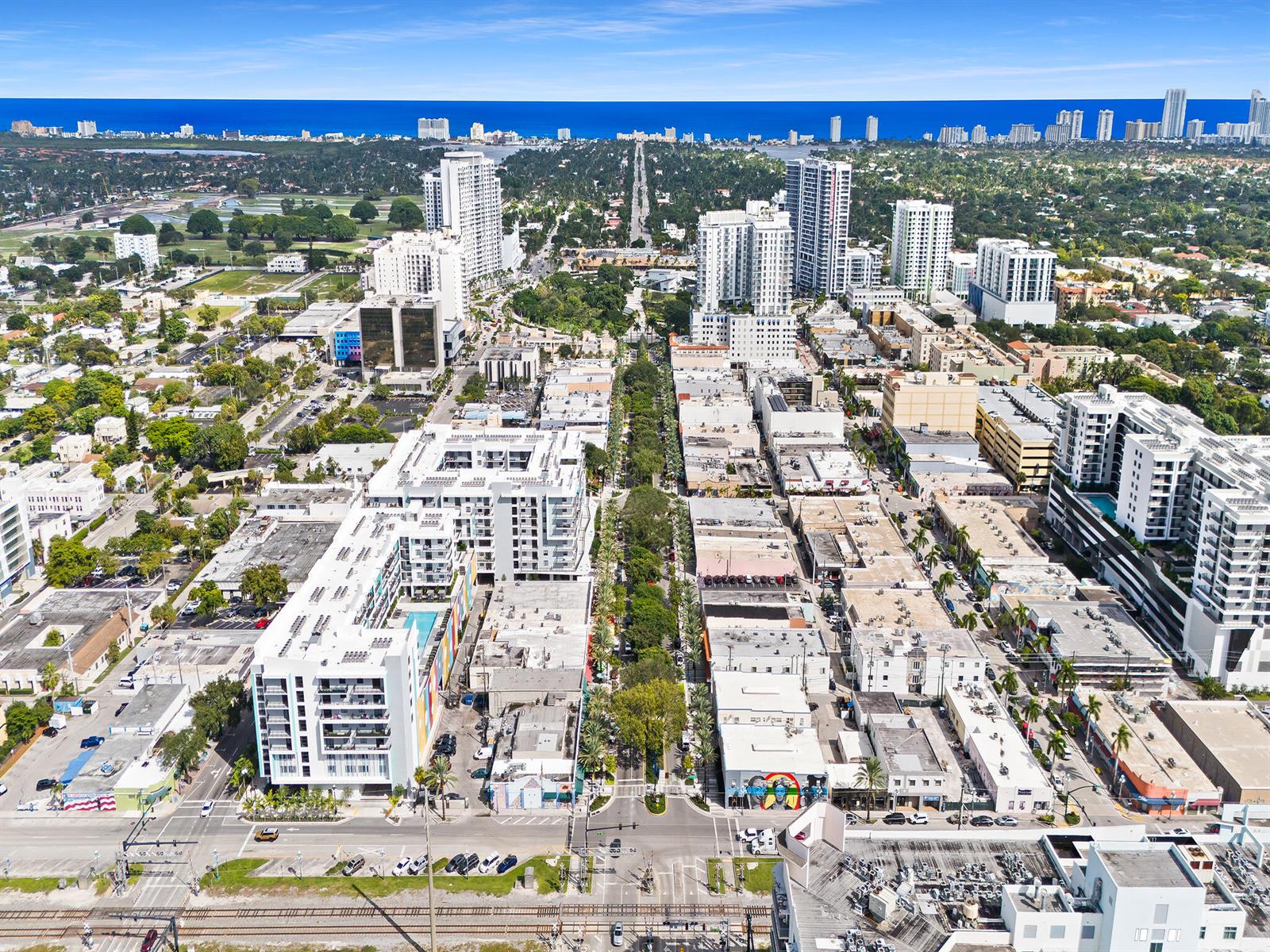 An aerial view shows a city street lined with buildings and trees leading toward the ocean — 2001 Hollywood Boulevard, Hollywood FL 33020, HOLLYWOOD, FL