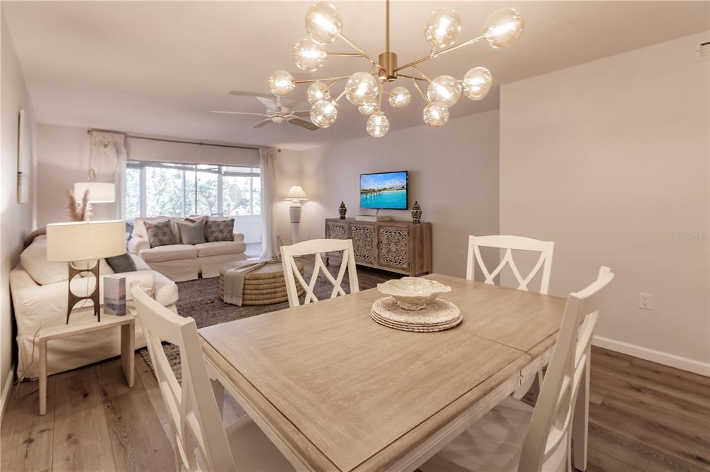 A dining area with a light wood table and white chairs opens into a living room — 1200 E PEPPERTREE LANE UNIT 303, SARASOTA, FL