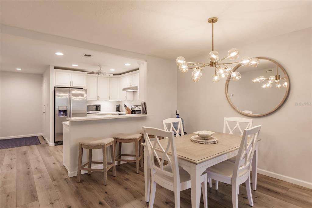 A dining area with a modern chandelier and mirror adjacent to an open kitchen — 1200 E PEPPERTREE LANE UNIT 303, SARASOTA, FL