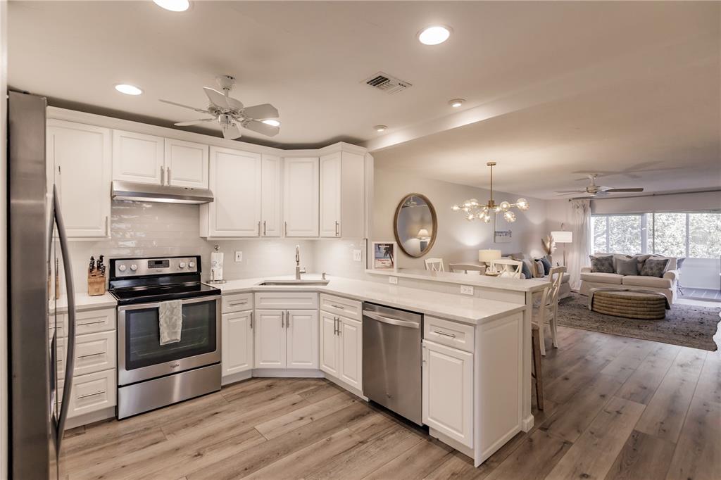 A kitchen with white cabinets, stainless steel appliances, and quartz countertops overlooks a living area — 1200 E PEPPERTREE LANE UNIT 303, SARASOTA, FL