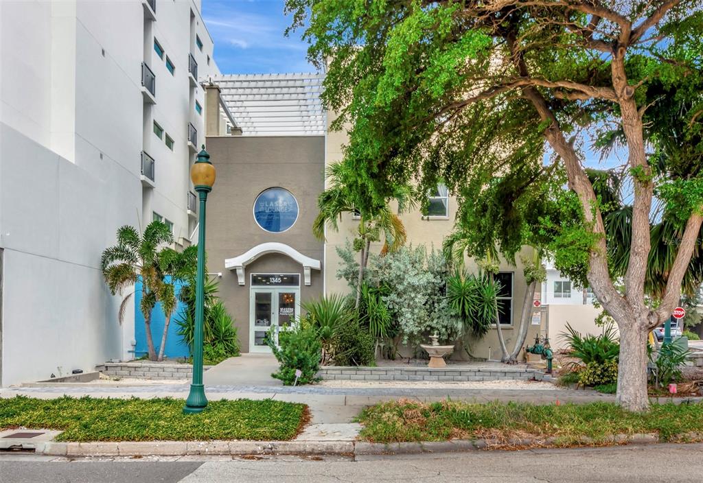 A two-story building with a circular sign and a front entrance sits behind a tree — 1345 2ND STREET, SARASOTA, FL