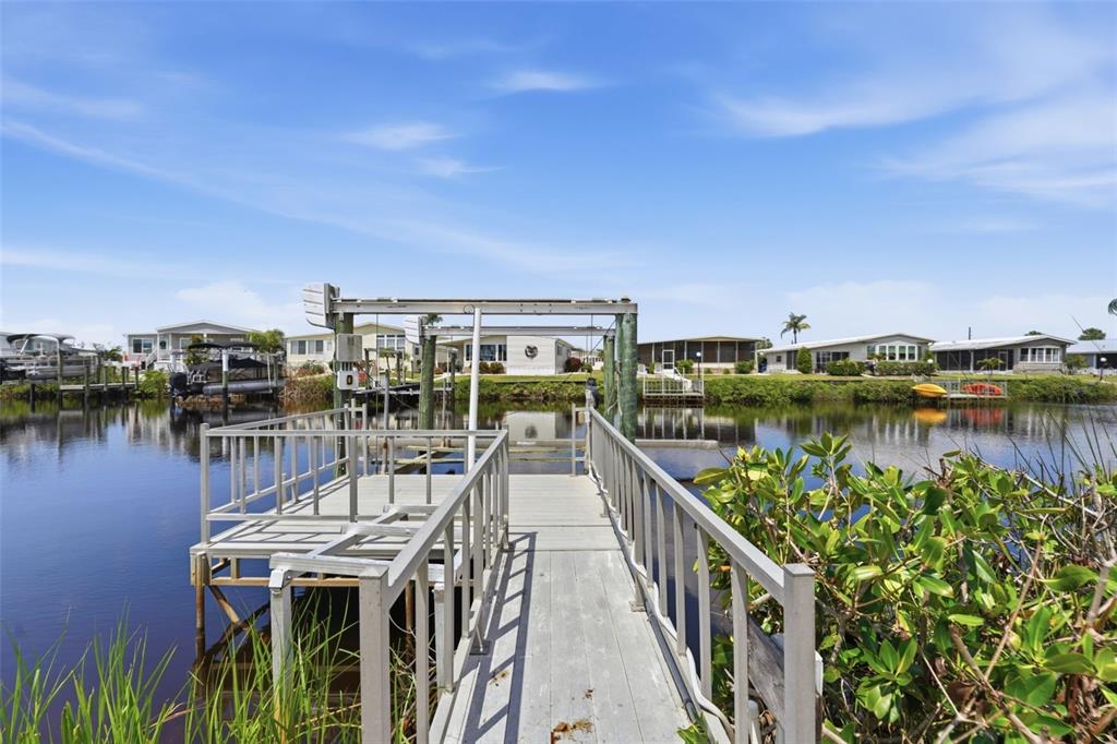A wooden dock with a boat lift extends over a canal toward several mobile homes — 118 MARTINIQUE ROAD, NORTH PORT, FL