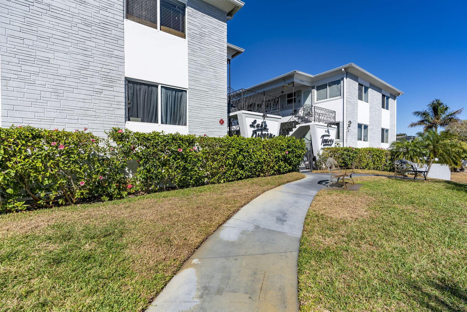 A sidewalk leads to the entrance of a two-story apartment building with landscaped hedges — 302 Lake Osborne Drive # 5, FL 33461, FL