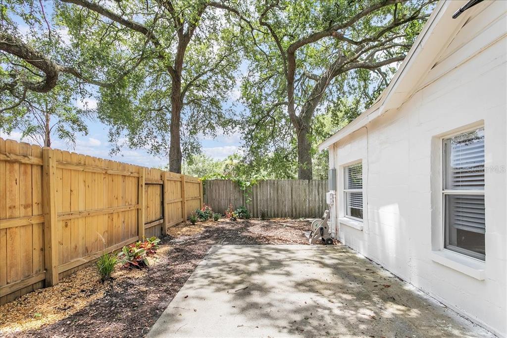A concrete patio sits beside a white house with a wooden fence and large trees — 6008 N TAMPA STREET UNIT 2, TAMPA, FL