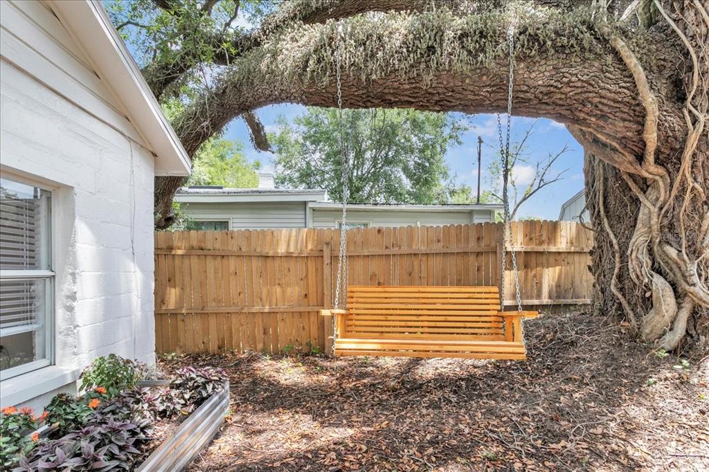 A wooden porch swing hangs from a large tree branch in a backyard with fencing — 6008 N TAMPA STREET UNIT 2, TAMPA, FL