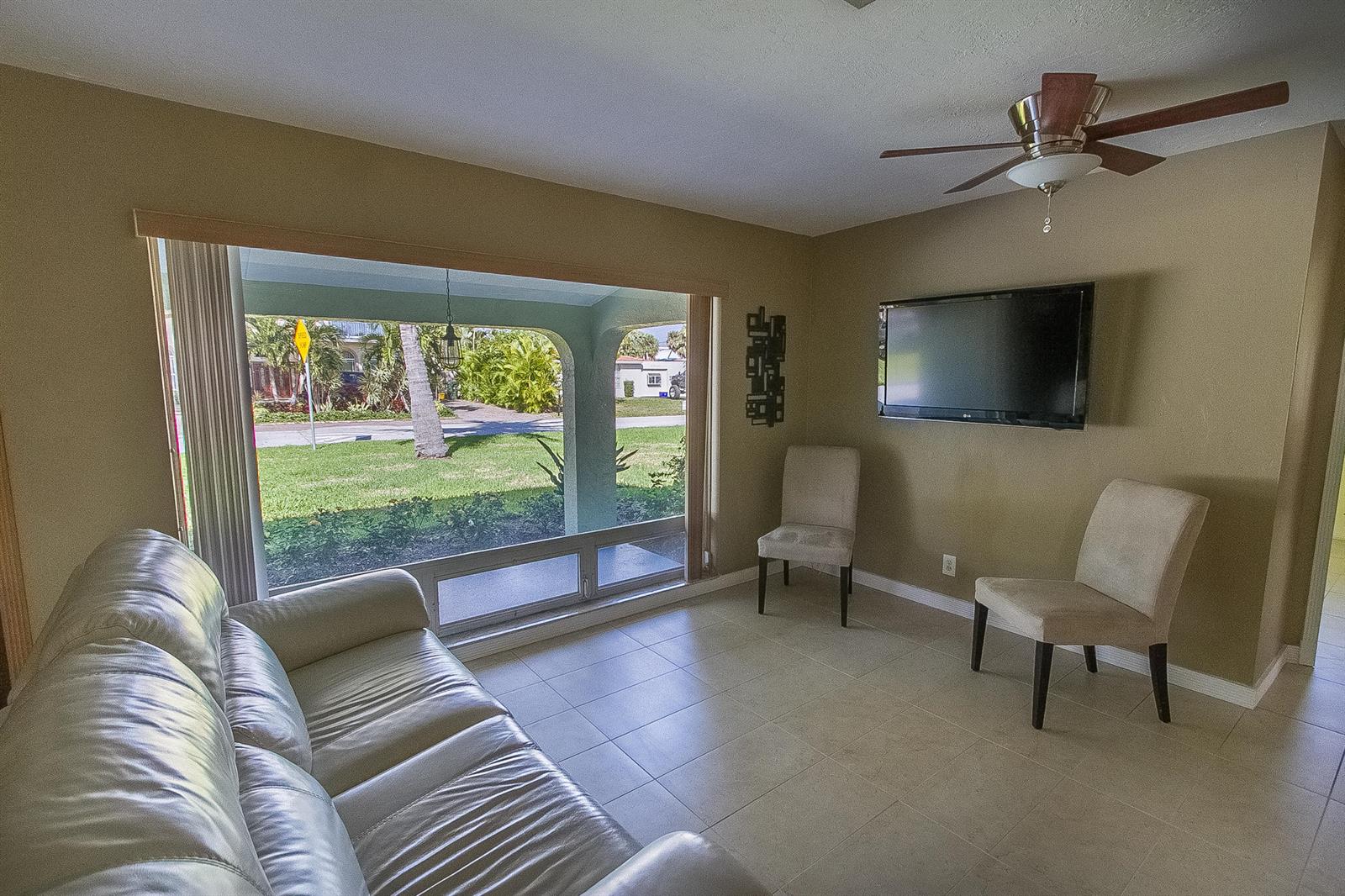 A living room features a large window, a wall-mounted television, two chairs, and tile flooring — 116 NW 8th Street, Boca Raton FL 33432, BOCA RATON, FL