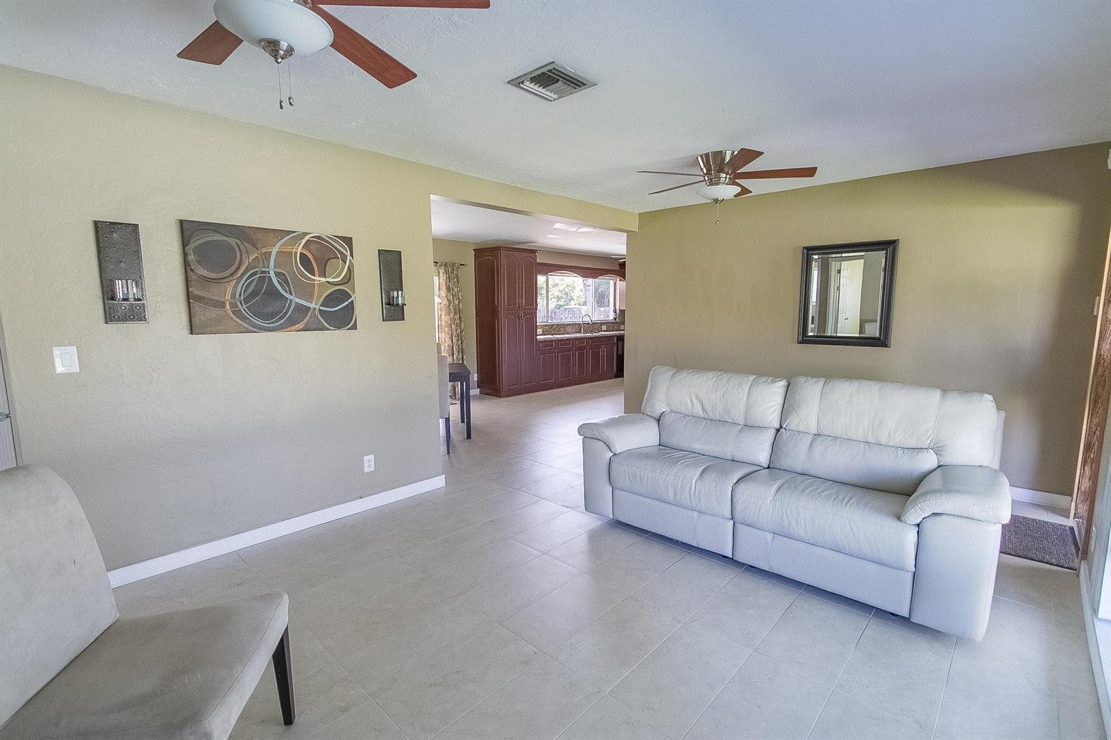 A living room with light-colored tile floors, a white sofa, and a view into the kitchen — 116 NW 8th Street, Boca Raton FL 33432, BOCA RATON, FL