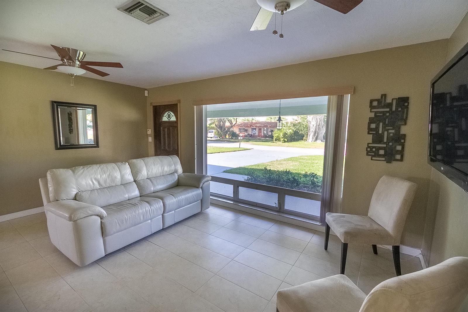 A living room features a white leather sofa, two beige chairs, and a large picture window — 116 NW 8th Street, Boca Raton FL 33432, BOCA RATON, FL