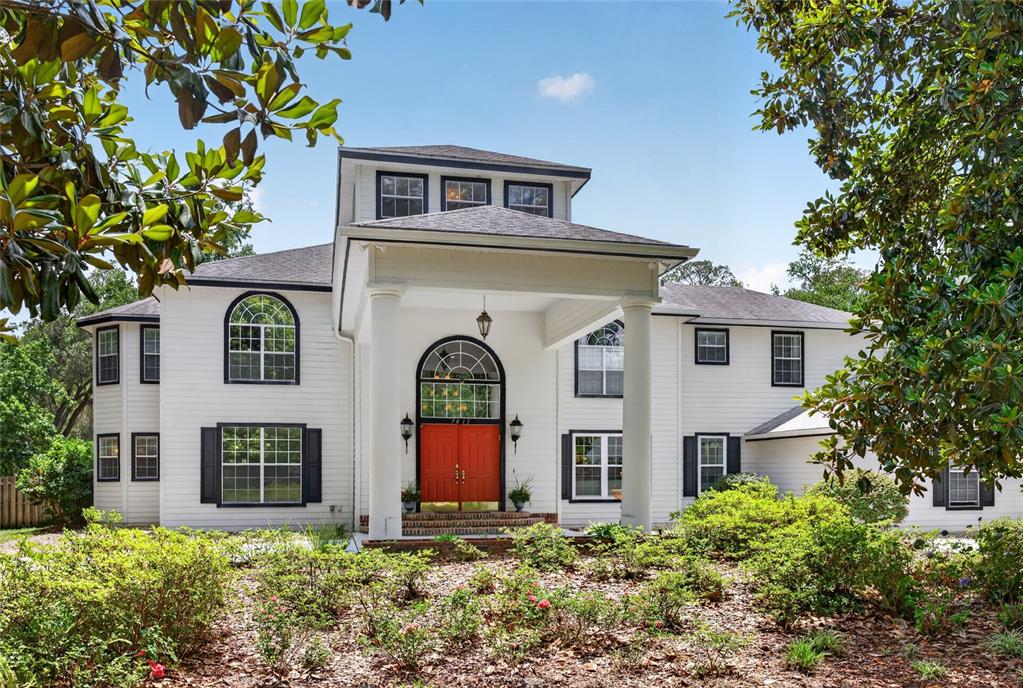 A two-story white house features a prominent portico with columns and a bright red door — 7815 NW 20TH LANE, GAINESVILLE, FL