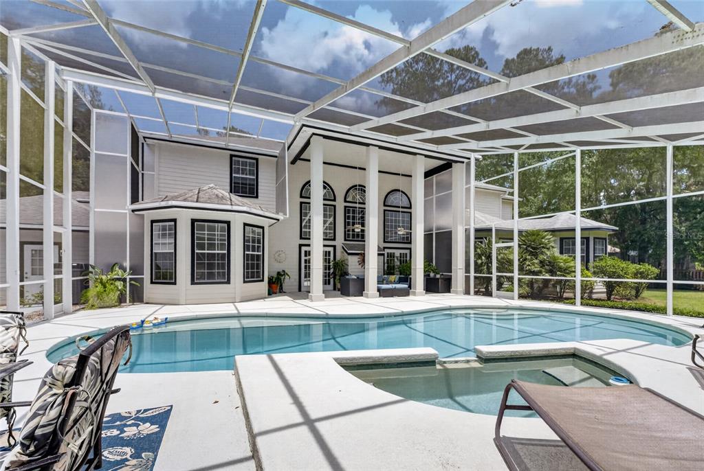A screened-in pool and hot tub area behind a two-story house with white siding — 7815 NW 20TH LANE, GAINESVILLE, FL