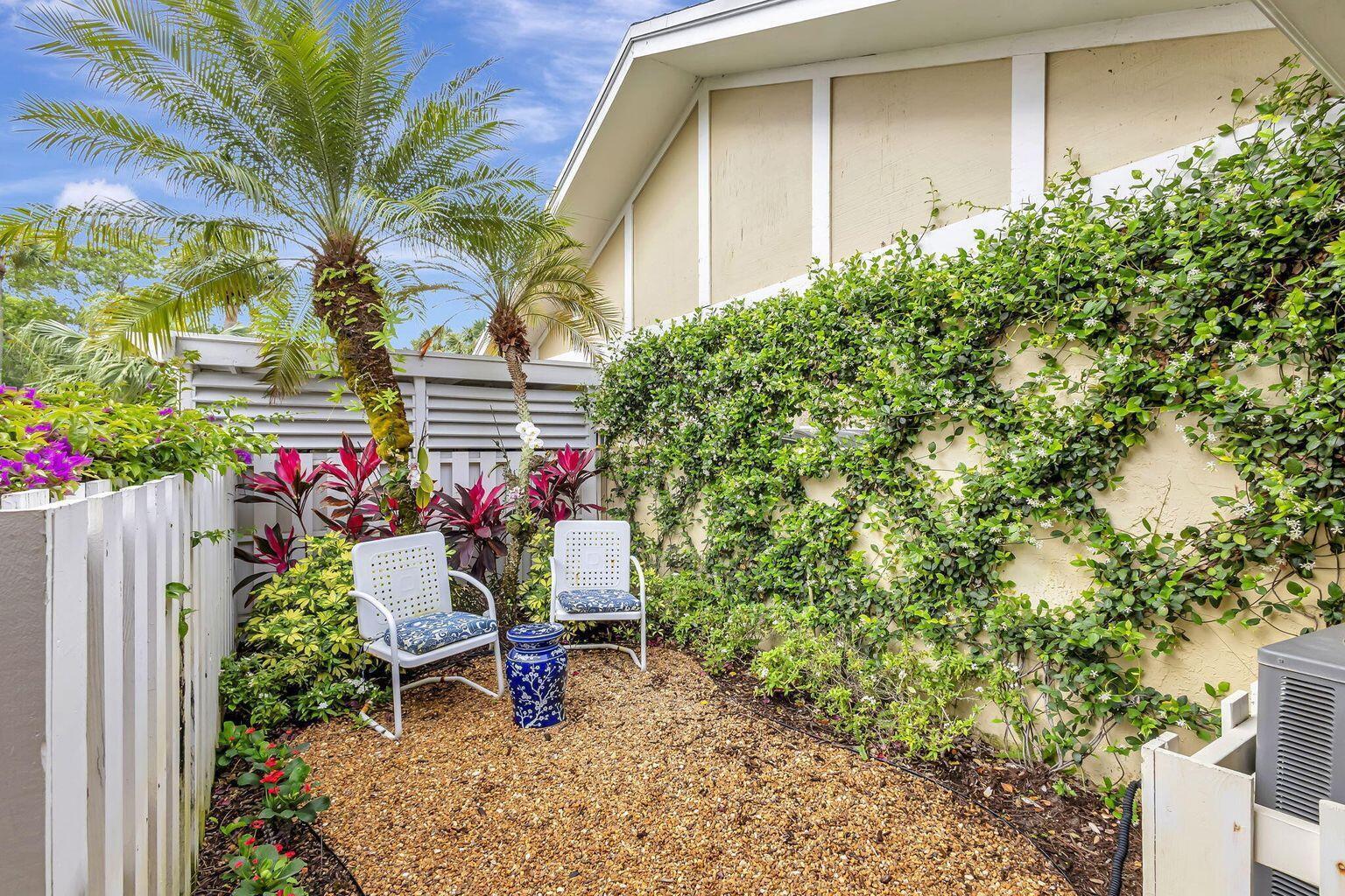 A small gravel patio features two white chairs, a blue garden stool, and climbing vines — 3667 Cape Pointe Circle, Jupiter FL 33477, JUPITER, FL