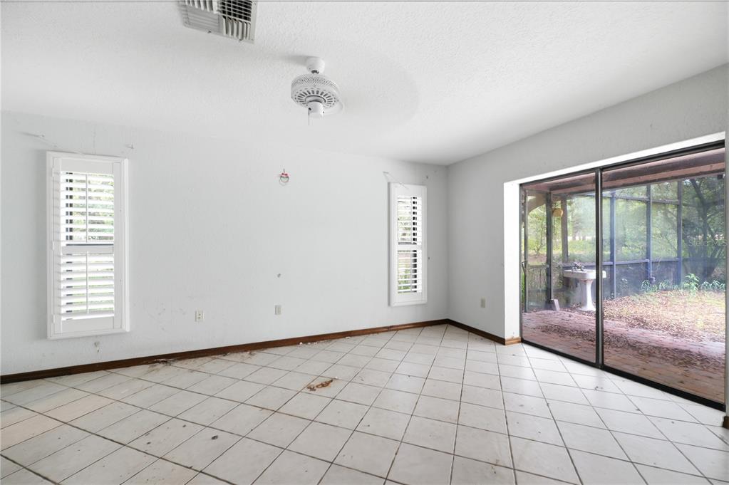 A room with white tile floors, white walls, plantation shutters, and a sliding glass door — 4444 RAINES ROAD, BROOKSVILLE, FL